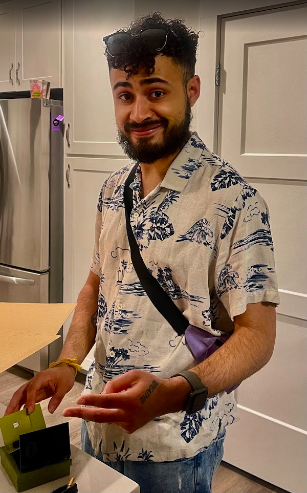 Angel in a patterned button-down and crossbody bag, photographed indoors.